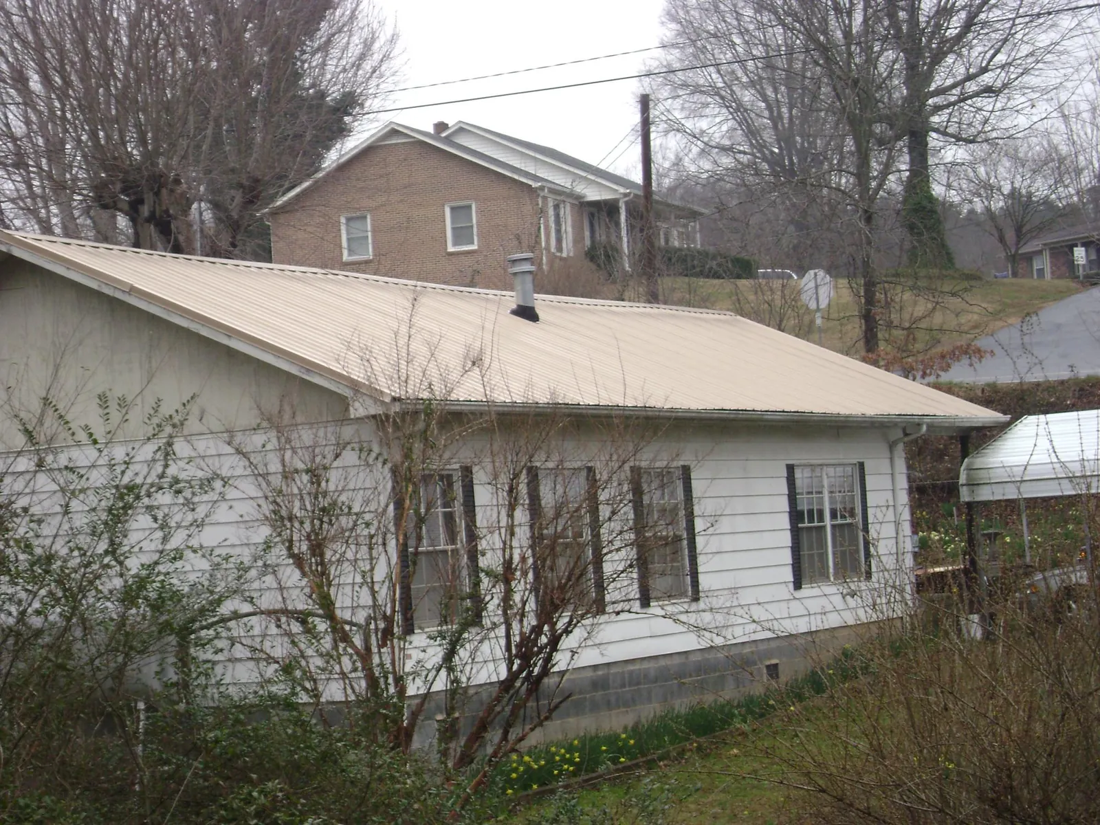 Tan metal roof on a white sided house set into a hillside — Commercial Roofing by Roofing Brothers in Lyndhurst